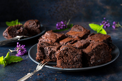 Chocolate Brownie Cakes on a dark background. In the photograph there are mint, cocoa powder and flowers.