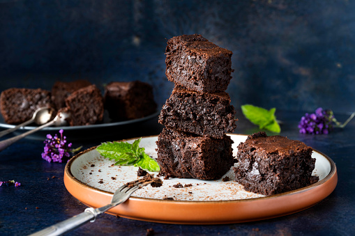 Chocolate Brownie Cakes on a dark background. In the photograph there are mint, cocoa powder and flowers.