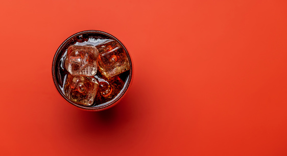 Refreshing glass of cola with ice. Over red background with copy space. Flat lay