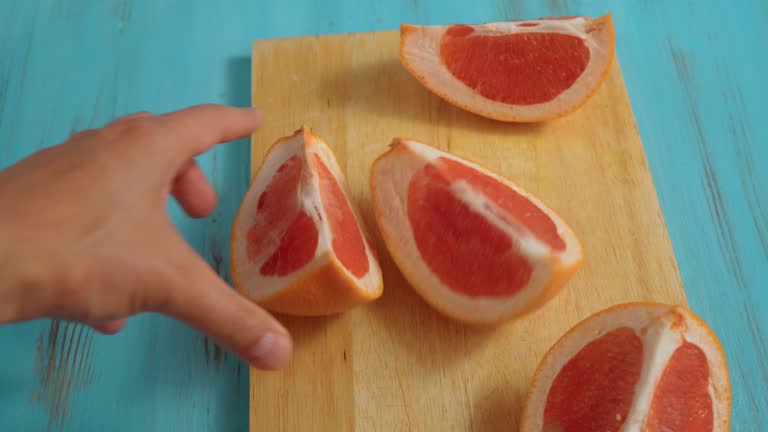 Cutting ripe grapefruit on board close-up. Citrus fruits, making fresh juice or tropical cocktails.