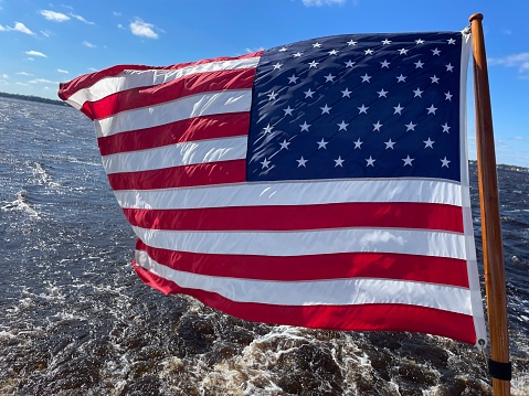 The starts and stripes is flying from a ship sailing the St John’s river in Jacksonville, Florida. The flag is clearly discernible with vivid colours Ann’s a green, river water background.