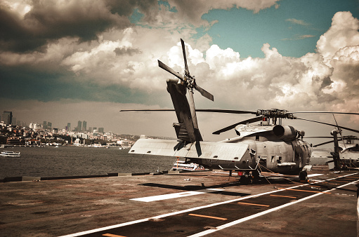 An armed guard looks up at the MV-22 Osprey aircraft while patrolling the deck of USS Tripoli (LHA 7) of the US Navy docked at Garden Island, Sydney Harbour.  This image was taken from Mrs Macquarie's Chair on an afternoon in Spring.