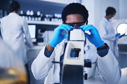 Microscope, science and black man working on test in laboratory of medical research analysis. Scientist, microbiology and biotechnology technician planning investigation, innovation and dna pathology