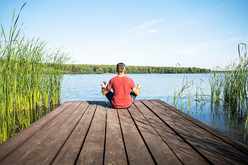 man practicing yoga meditation and breathwork outdoors by the lake.