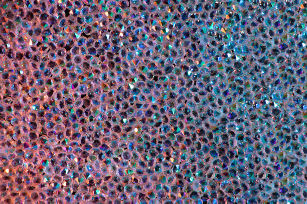 istock Abstract rhinestones background. Texture of rhinestones illuminated with multi-colored light. Pink and blue shine diamonds. Close up. Flares on glass 1569229078