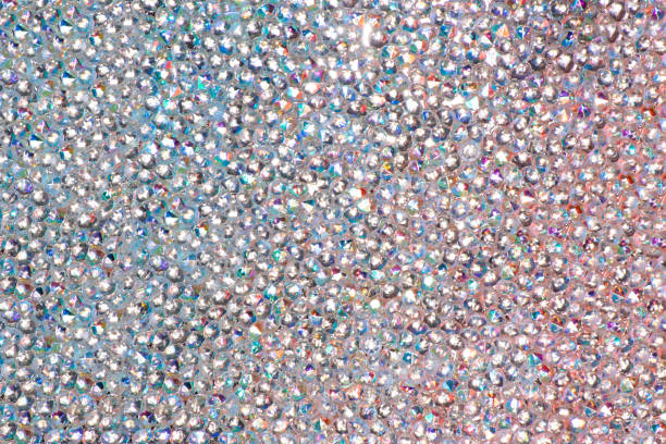 istock Abstract rhinestones background. Texture of rhinestones illuminated with multi-colored light. Pink and blue shine diamonds. Close up. Flares on glass 1569229089