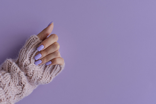 Mano de hembra con manicura gelish. Uñas de color lavanda de moda sobre fondo púrpura, espacio de copia photo