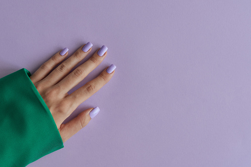 Manicura gelish con uñas moradas sobre fondo de color lavanda. Uñas moradas y ropa verde photo