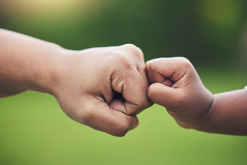 Fist bump, hands of baby and father together for gesture of support, success or trust in family on green blurred background. Hand, bumping fists and dad with son or sign of solidarity or celebration