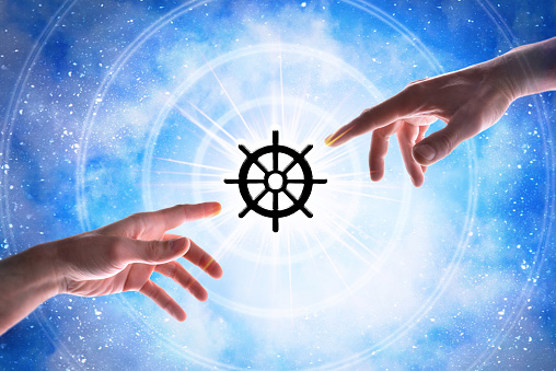 Hands pointing wheel of dharma symbol of the Buddhist religion with concentric circles with a flash of light on a magical starry bluish background of the universe.