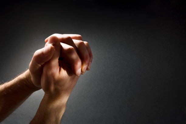 Praying man hands with interlocked fingers isolated dark