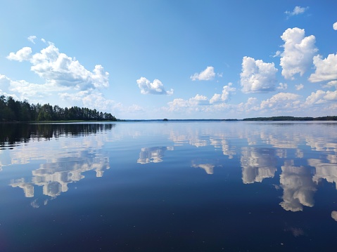 Warm sunny July day at Lake Saimaa in Finland. Fluffy white clouds and blue sky reflecting on almost mirror like water surface. Islands seen in the the horizon.