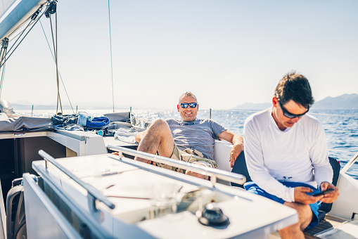 Businessman working with smart phone while other crew member posing for a photo on sailboat.