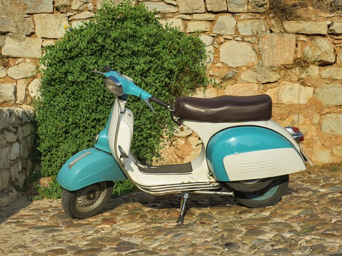 Parked scooter in front of a stone wall with a creeper