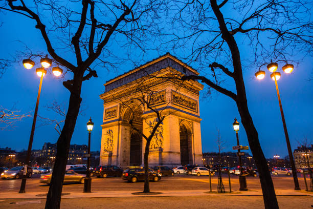 триумфальная арка этуаль на освещенной площади шарля де голля в париже, франция - paris france night charles de gaulle arc de triomphe стоковые фото и изображения