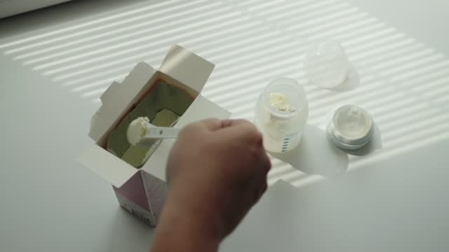 Pouring milk formula into a baby bottle with water for preparing baby food, close-up.