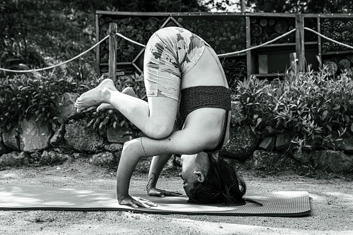 side view of an athletic young woman standing headfirst on a yoga rug in a garden | asana | healthy lifestyle