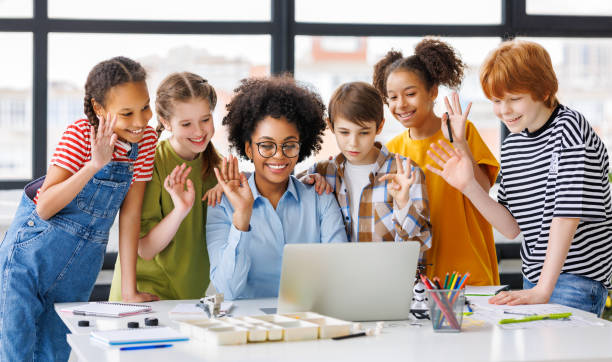 istock Teacher and students watching laptop screen and waving during a video conference 1569379387