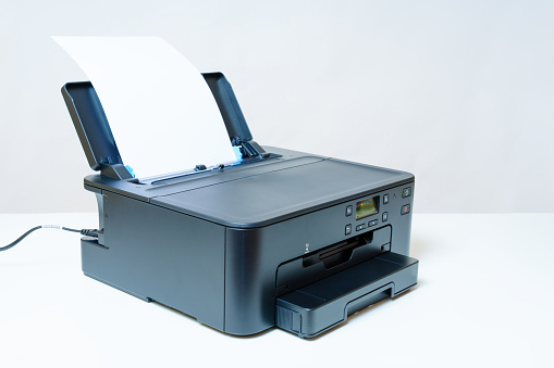 Side view of an inkjet printer having a sheet of paper neatly installed in the rear tray ready to start the job.