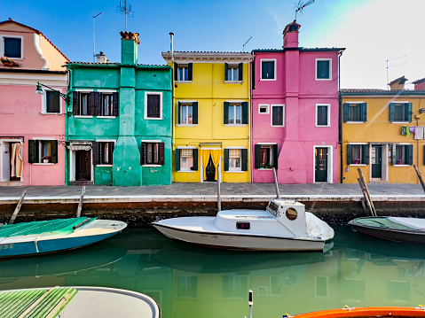 Colorful canal houses and boats on Burano island in the Venetian Lagoon. A Venice landmark in northern Italy. Vessel and buildings reflecting in calm water. Beautiful poster like travel and tourism background on a sunny day with copy space.