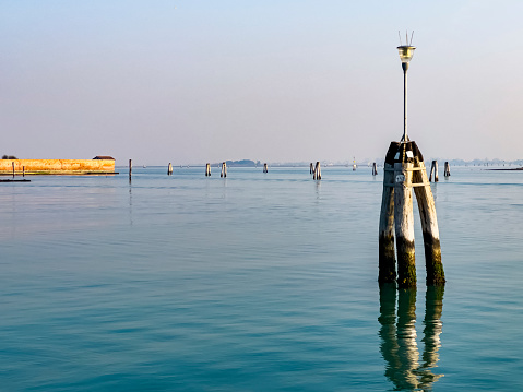 Venice lagoon with three big wooden poles implanted in the seabed called Briccola or Bricola (Dolphin), used to indicate the viable routes in the sea to boats. Veneto, Italy, Europe.