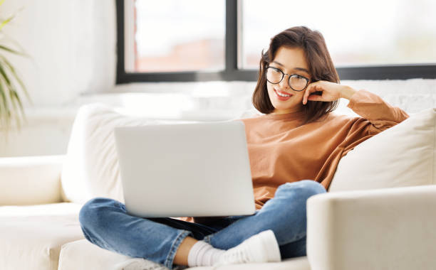 istock beautiful young woman uses laptop while sitting on sofa 1569413576