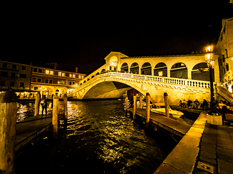 View of illuminated buildings and Rialto Bridge, Ponte di Rialto over Grand Canal at night in Venice, Italy, in late evening; bridge and buildings reflected in water. Travel destination background with copy space.