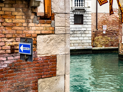 Blue directional way sign with arrow pointing into one direction in Italian language at an empty canal in Venice, in Italy. Travel destination background with copy space.