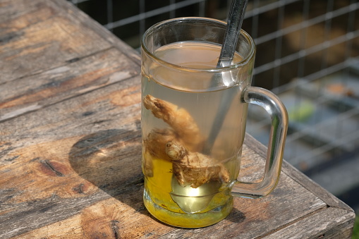 Wedang Jahe Gula Batu, Hot Liquid Ginger is a traditional Indonesian drink made from ginger, rock sugar, and hot water. Indonesian Drinks. Served in a clear glass on a brown rustic wooden table.