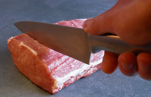 The chef is cutting fresh raw meat into steaks. Close-up on a gray background.