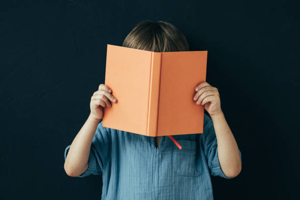 istock Little boy reading a book on stand up front of black board 1569479548