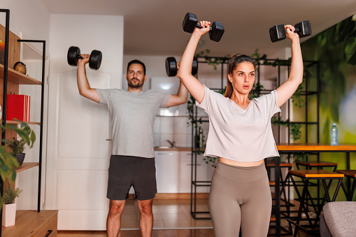 Active young couple doing biceps exercises using dumbbells while working out together at home