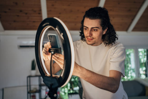 istock Male influencer vlogging through mobile phone with ring light at home 1569502176