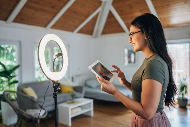 istock Female influencer vlogging through mobile phone with ring light at home 1569505517