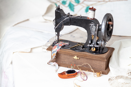 Still life with a sewing machine. Vintage sewing machine, scissors and a piece of fabric. Nearby is a decorative ceramic needle bed in the form of a Dutch shoe.