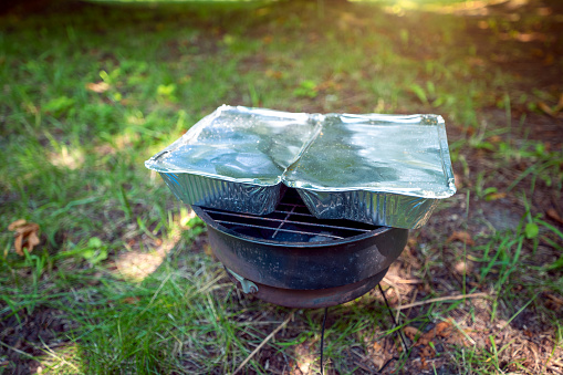 Old small rusty grill spread out on the grass in the park. The perfect outdoor grill. On the grill, 2 aluminum trays with food inside