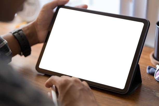 istock Over shoulder view of young man using digital tablet on white table at home office. 1569541556