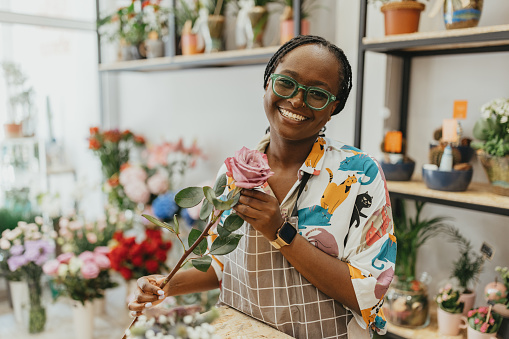 Young female entrepreneur holding flower looking at camera and smiling. This photo is a part of the day in the life series.