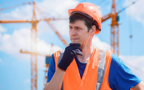 istock Portrait of builder in hard hat and vest at construction site. Young caucasian builder with thoughtful expression. Thoughtful male handyman 1569565498