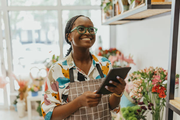 una empresaria afroamericana de 27 años es dueña de una floristería fresca, utilizando una tableta digital. - pequeña empresa fotografías e imágenes de stock