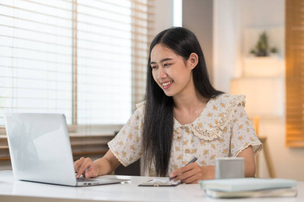 istock Beautiful young woman using laptop and making notes on notebook. 1569585896