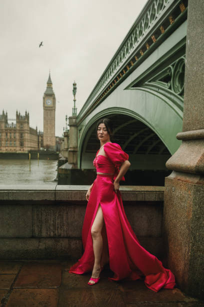 elegante modelo posando con vestido rosa en el icónico puente de westminster con el big ben y el edificio del parlamento de fondo en un día ventoso y lluvioso - london england thames river storm rain fotografías e imágenes de stock