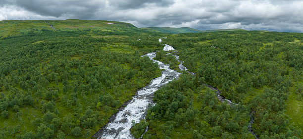A raging river with waterfalls runs through deep green alpine forest landscape. Seen from above in the village of Funasdalen, Harjedalen, Sweden.