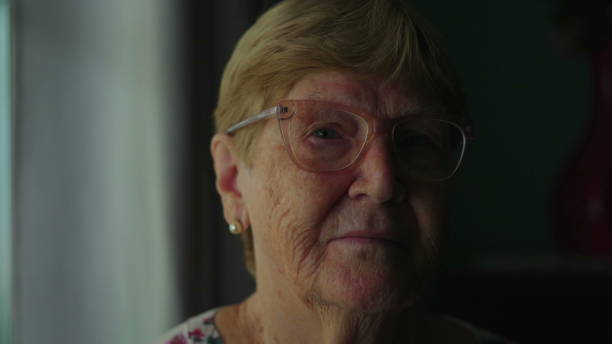istock Elderly senior woman close-up face looking at camera with serious expression, dramatic lighting of older female person in 80s depicting old age and experience 1569634867