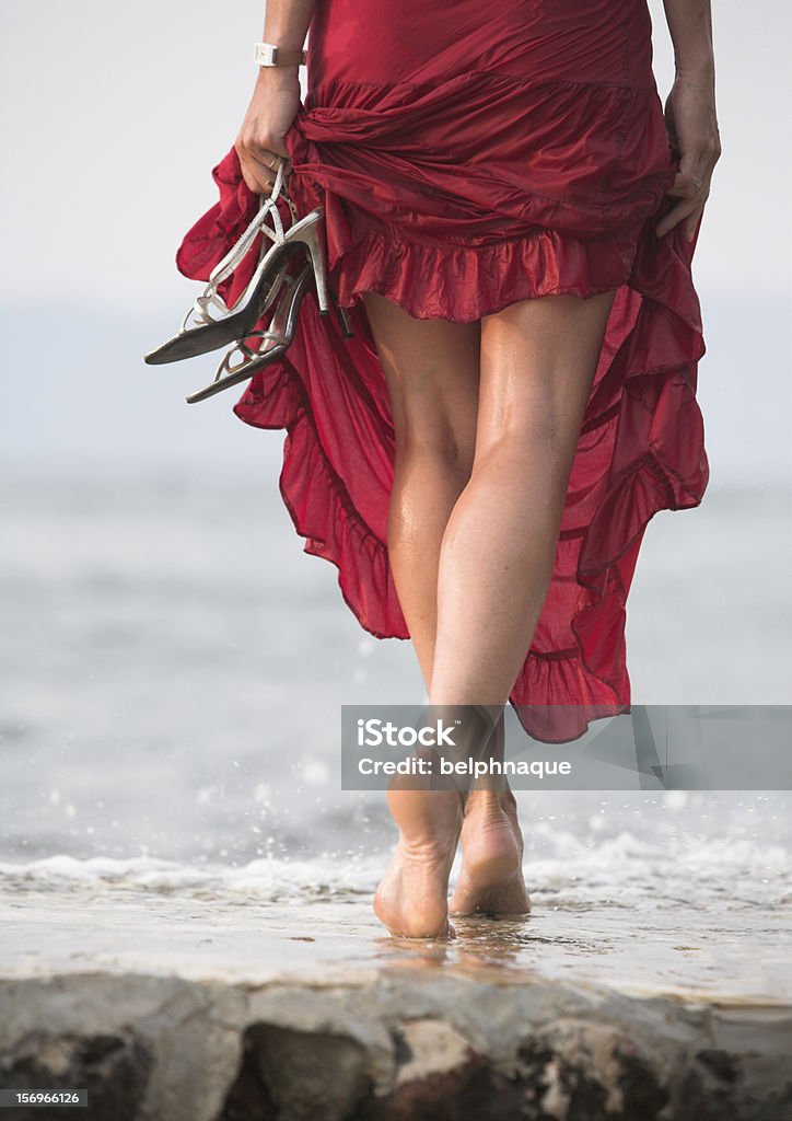 Sexy red dressed woman walks, wet stone, sea Wet ground, woman legs, walk on beach rocks Adult Stock Photo