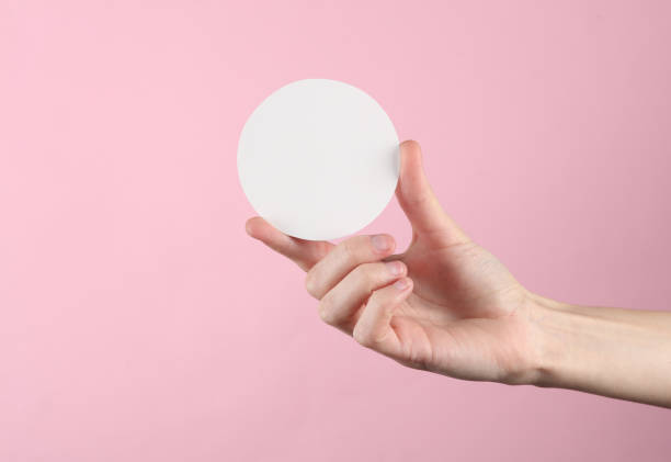 istock Female hand holds a white empty circle for text, pink background 1569664292