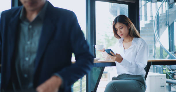 istock Young Asian businesswoman using smartphone at table in cafe 1569665368