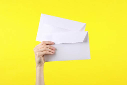 female hand holds two white envelopes on yellow background