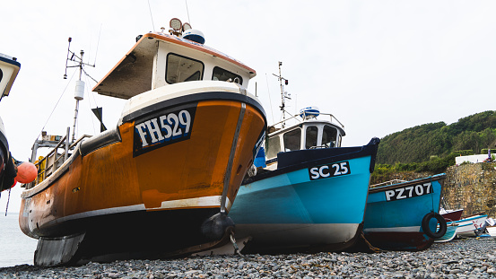Cadgwith, Cornwall, UK - July 1, 2023.  Traditional Cornish fishing boats out of the water and on the pebble beach at the popular tourist destination of Cadgwith in Cornwall