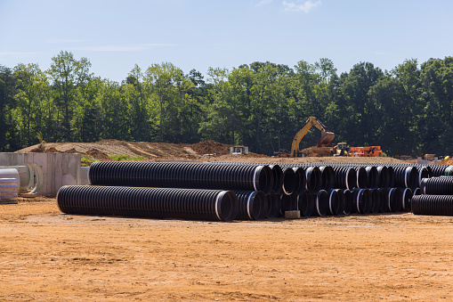 On construction site, stacks of large black plastic pipes ready for sewerage installation.